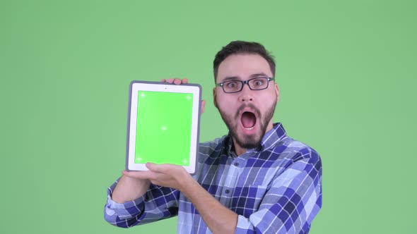 Happy Young Bearded Hipster Man Showing Digital Tablet and Looking Surprised