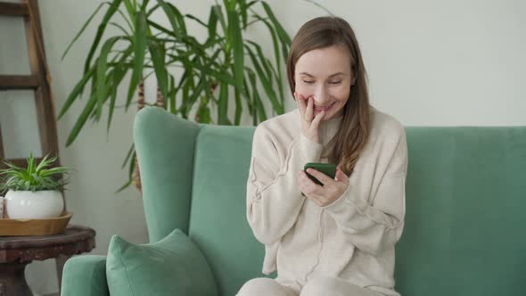 Young Woman Using Phone Celebrating Online Lottery Win Reading Good Messagesitting on Sofa at Home