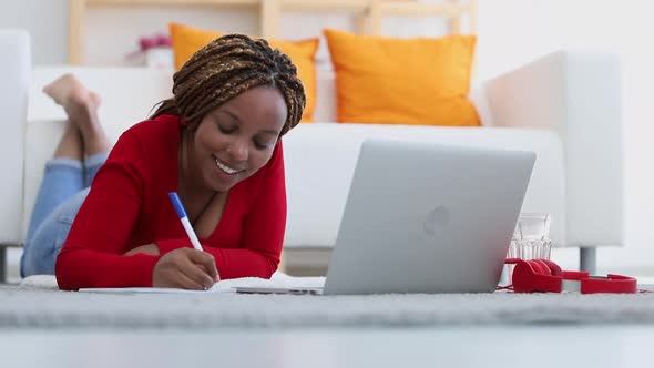 Beautiful Young Young Woman Writing and Using Laptop While Lying on Floor at Apartment Room Spbi