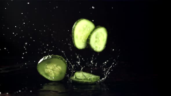 Pieces of Fresh Cucumber Fall on the Table with Splashes of Water