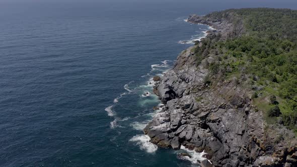 Drone flying around a cliff off the rocky coastline of a small island in Maine