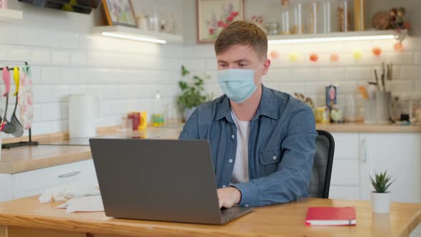Caucasian man with a medicinal mask on face is working from home at the laptop