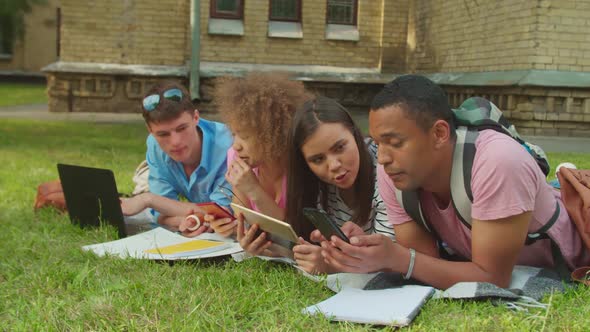 Group of Mixed Race Cheerful Students Using Gadgets to Learn Outdoors