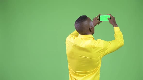 Rear View of Young African Businessman Wearing Yellow Shirt Taking Picture with Phone