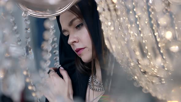 Pretty Woman with Big Blue Eyes is Posing in Room with Bright Crystals Wearing Black Hood