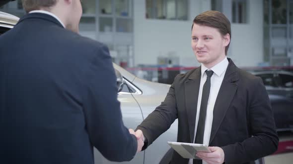 Portrait of Brunette Caucasian Blue-eyed Trader in Business Suit Shaking Client's Hand and Talking