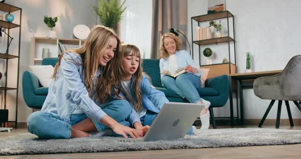 Woman Reading Book on the Couch while Her Active Friendly Eldest and Younger Daughters Playing