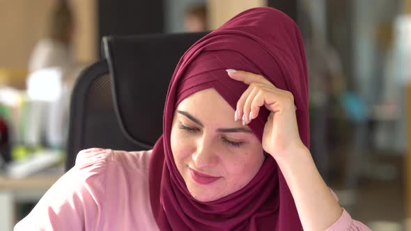 Portrait of a young attractive smiling Muslim woman in a hijab at the workplace in the office