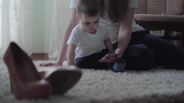 Young Woman Sit on the Floor with a Small Baby Boy and Show Him Cartoon at Mobile Phone