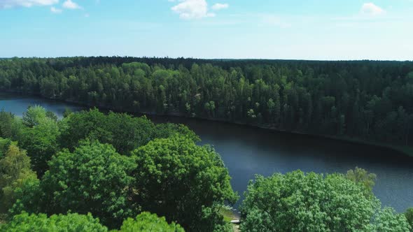 Droneing forward along a Swedish dark blue river surrounded by green forest on a summer day.