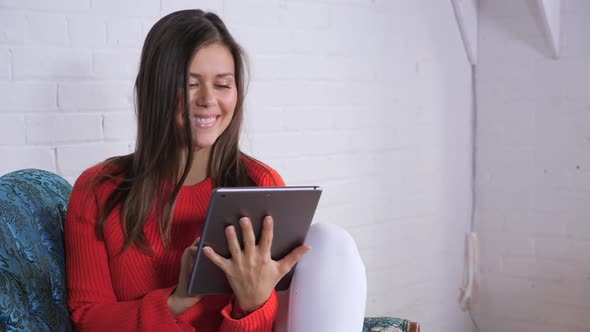 Attractive Young Female In Front Of A White Brick Wall While Playing On Her Tablet 1