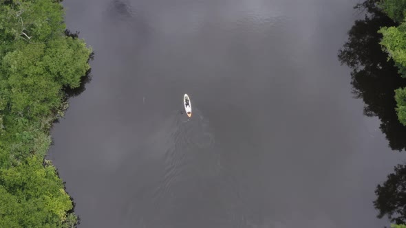 Vertical aerial tracks person paddleboarding on small rural river