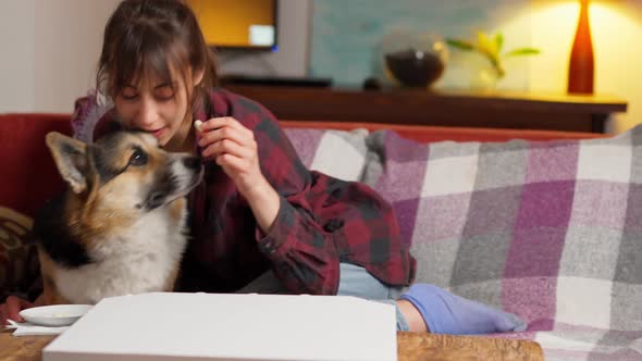 Tender Woman Sits on Couch with Dog Hugging and Feeding Him