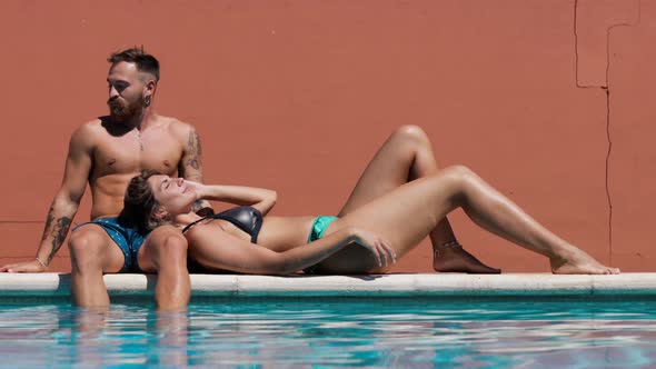 Couple in swimwear resting on poolside