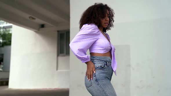 Gorgeous Curly-haired African-American Woman Posing and Dancing on the Street Against a Wall.