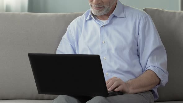 Aged man sitting on couch, using laptop, working from home, engineering project