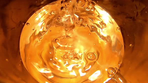 Golden effect of water being poured into glass. Top view, close up