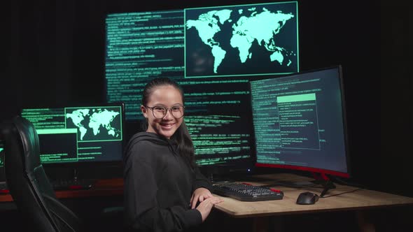 Asian Young Girl Hacker Hacking With Multiple Computer Screens And Smiling To Camera In Dark Room