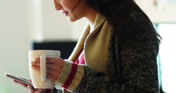 Woman having coffee while using mobile phone