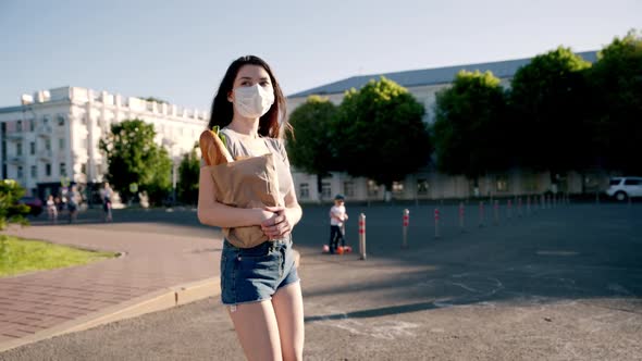 Caucasian Young Pretty Woman Delivery Worker in Medical Mask Walking the Street and Carrying Packet