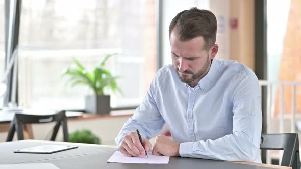 Disappointed Young Man Trying To Do Paperwork in Office 