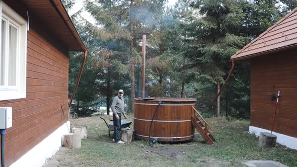 Man Alight The Fire For Traditional Hot Tub Between The Wooden Houses