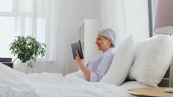 Old Woman with Tablet Pc Having Video Call in Bed