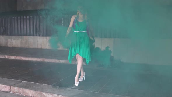 Cute Girl in a Green Dress with African Braids and Colorful Makeup Posing with Bright Green Smoke on