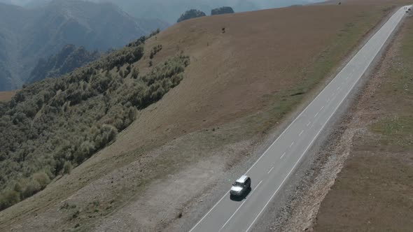 Tourist Car Moving on Mountain Road on Snowy Elbrus Landscape. SUV Car Driving on Highway in