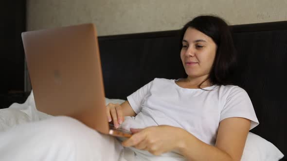 Smiling Woman Working on Laptop in Bed