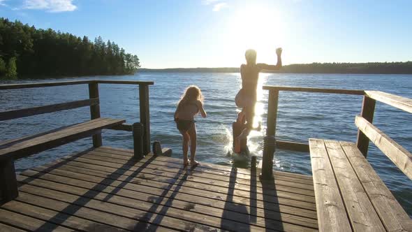 Family Couple with Daughter Running on a Wooden Pier and Jumping Into the Lake