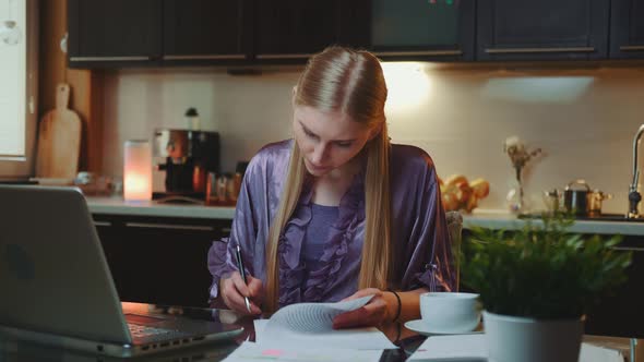 Blonde Business Woman in Bathrobe Signing Documents in the Kitchen at Home