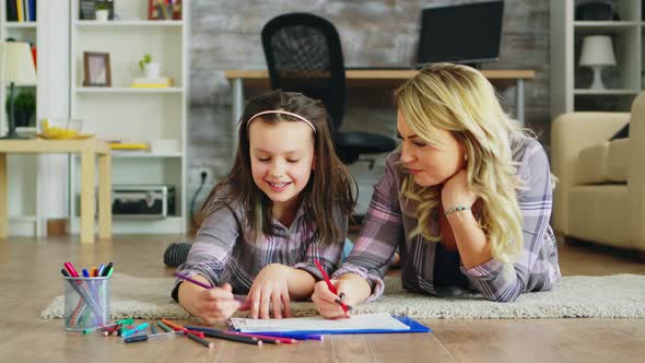 Cheerful Little Girl Lying on the Floor with Her Mother Drawing