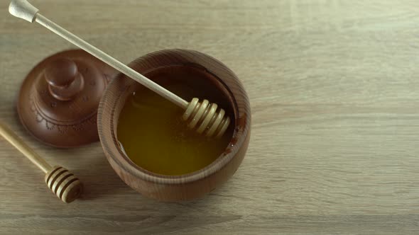 Honey with Wooden Honey Dipper in Wooden Bowl on Wooden Table