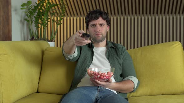 Young Man Sitting on Home Yellow Sofa Watching TV and Eating Popcorn Enjoying Comedy Movie