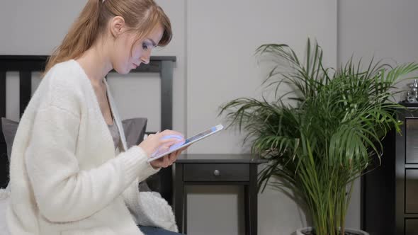 Woman Sitting on Side of Bed Using Phone for Internet