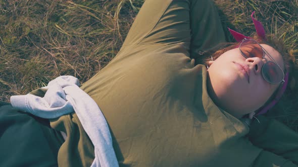 Plump Girl Hiker Lies on Grass at Campsite in Evening