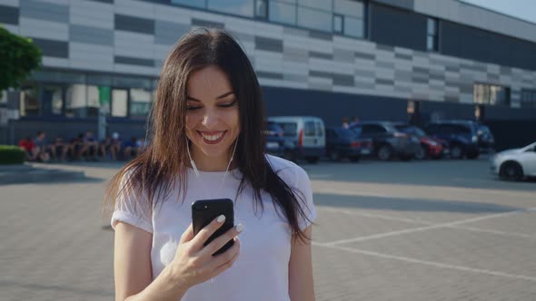 Portrait Trendy Millennial Young Woman in Headphones Uses a Smartphone on a Urban Background