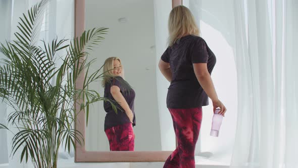 Blonde Confident Overweight Woman Walks to a Mirror and Smiling to Herself in the Reflection