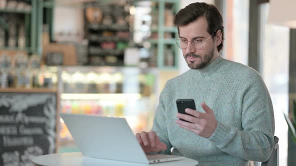 Young Man Laptop Checking Smartphone Cafe