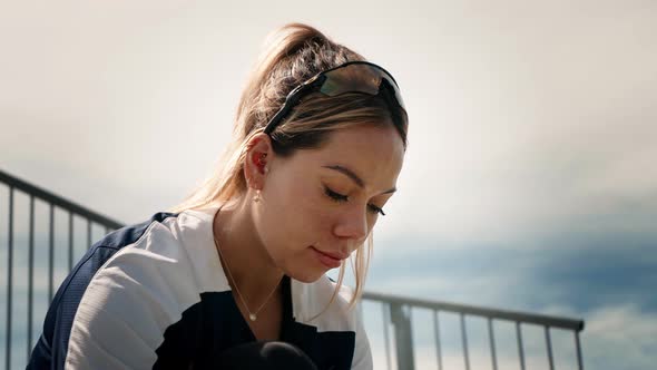 Female athlete is looking intensely down as she laces her shoes while sitting on a row of bleachers.