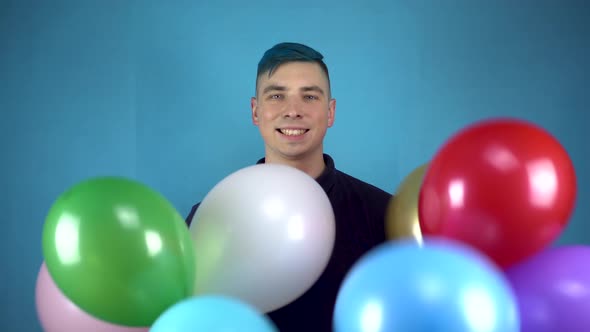 A Young Man with Blue Hair Holds in His Hands Colorful Inflatable Balls. Alternative Man Smiles with