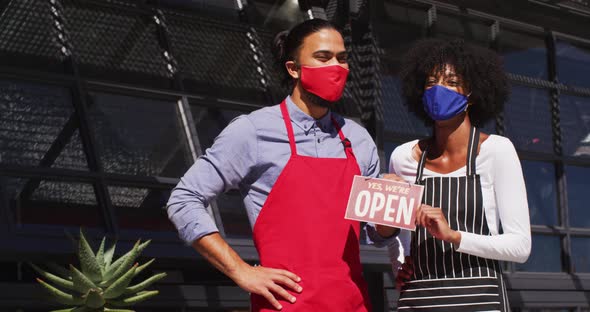 Diverse cafe workers wearing face masks showing were open signage
