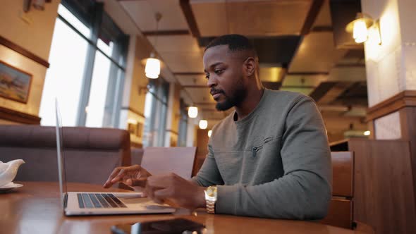 African American Man Online Working By Laptop in a Cafe