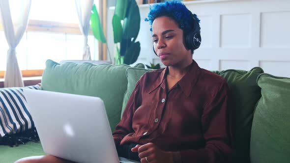 Young Attractive African American Woman in Headphones Sits on Couch with Laptop