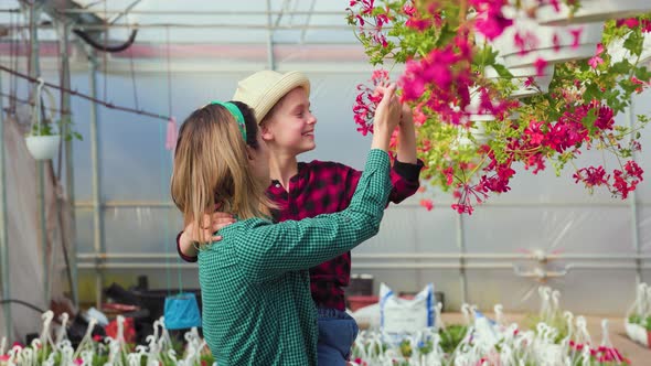 Woman with Happy Daughter in Her Arms Explains the Importance of Caring for Flowers in Greenhouse