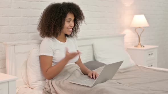 Video Chat on Laptop By Young African Woman in Bed