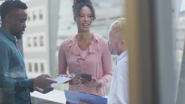 Diverse business people discussing with tablet and documents in creative office