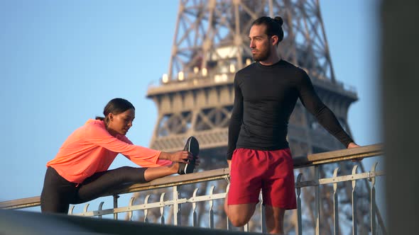 A couple stretching before running across a bridge with the Eiffel Tower