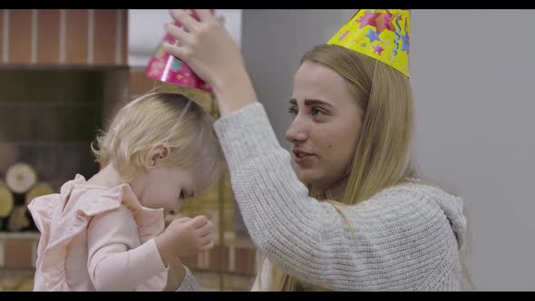Young Caucasian Woman Putting Party Hat on Little Girl's Head
